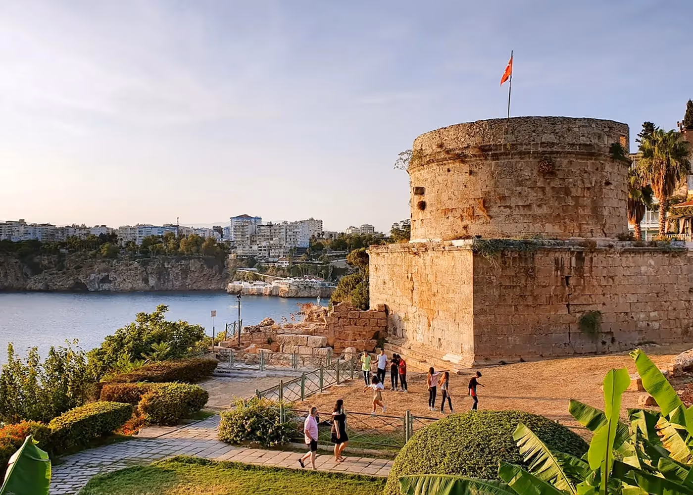 Ronde verdedigingstoren van grijze steen, omringd door palmen en gras in een park in Antalya