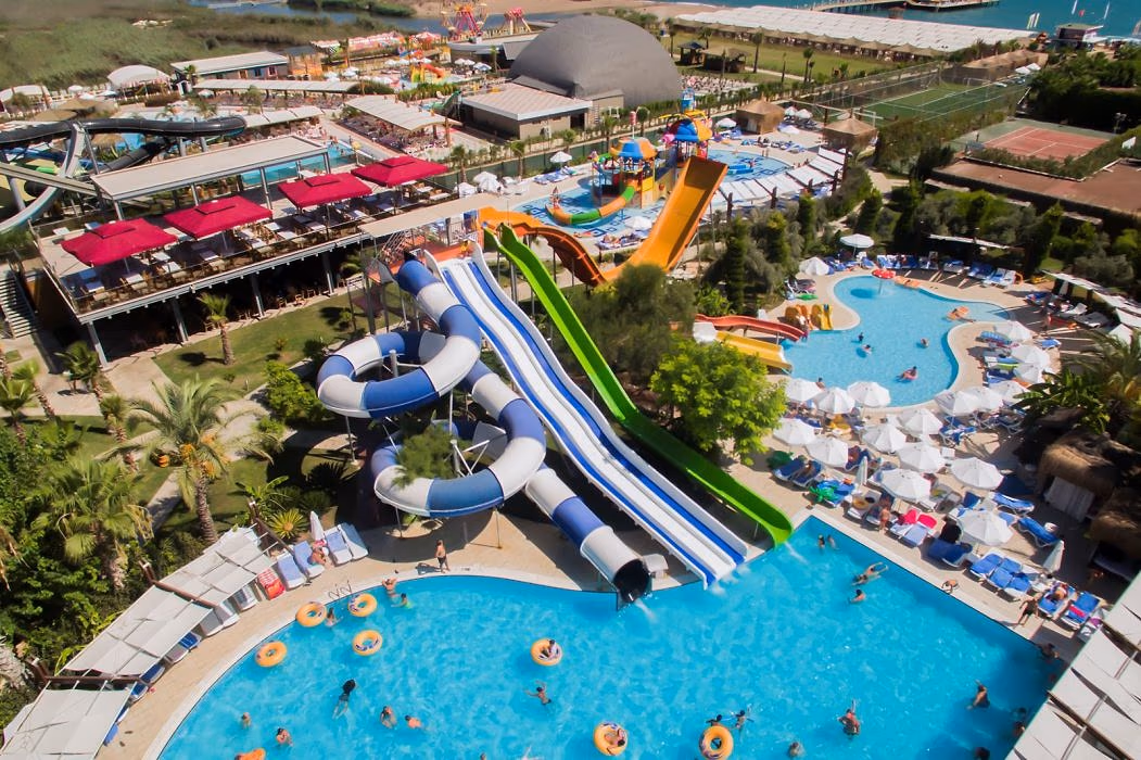 Zwembaden met blauwe en groene glijbanen en een terras met rode parasols bij Saturn Palace Resort, van bovenaf gezien