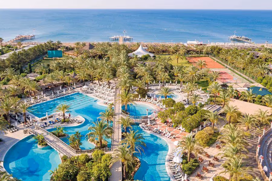 Zwembaden tussen de palmbomen van Hotel Royal Wings in Lara, van boven gezien met de zee erachter