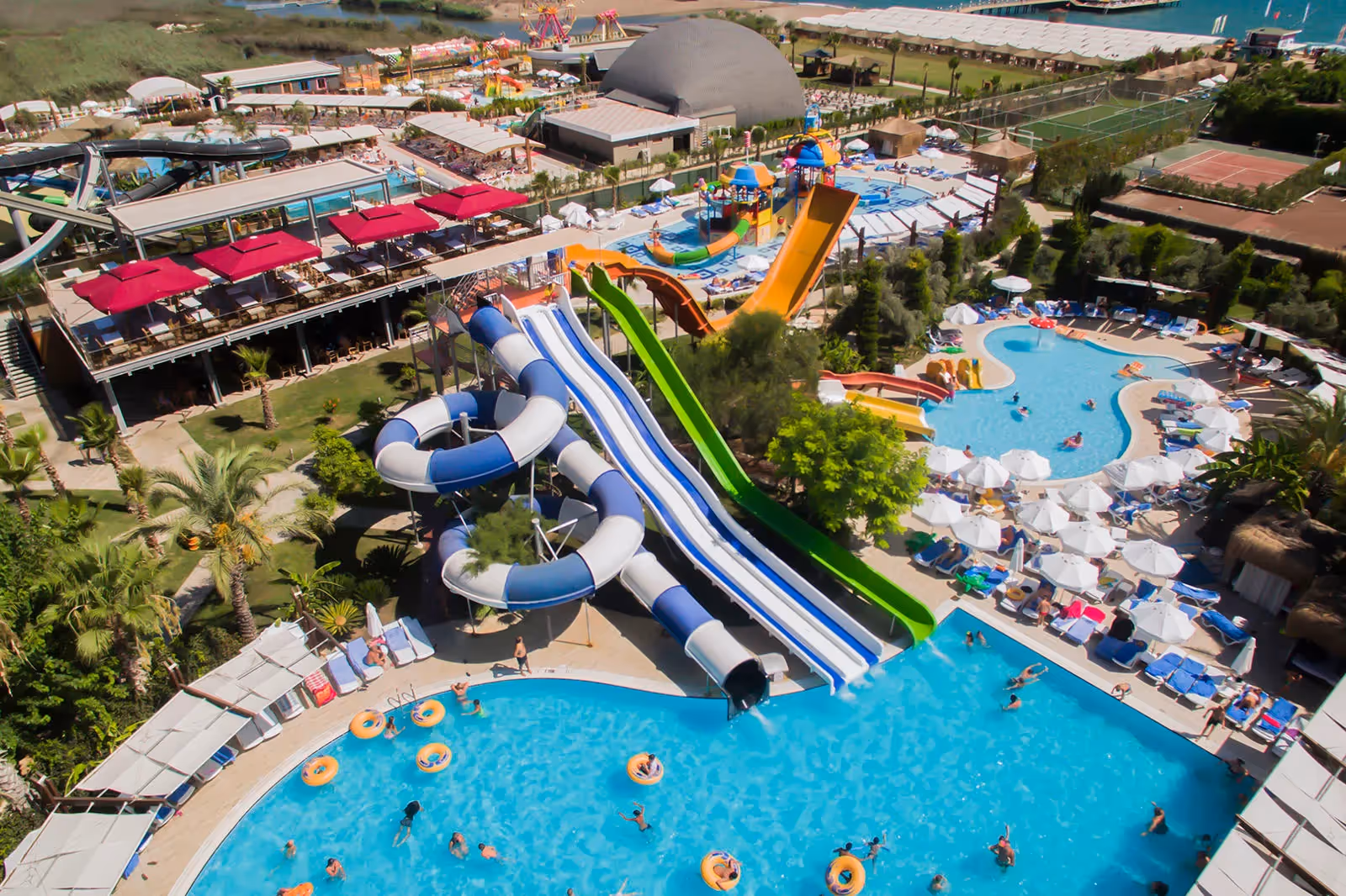 Luchtfoto van de kronkelende glijbanen boven een groot zwembad met zwemmers bij Saturn Palace Resort