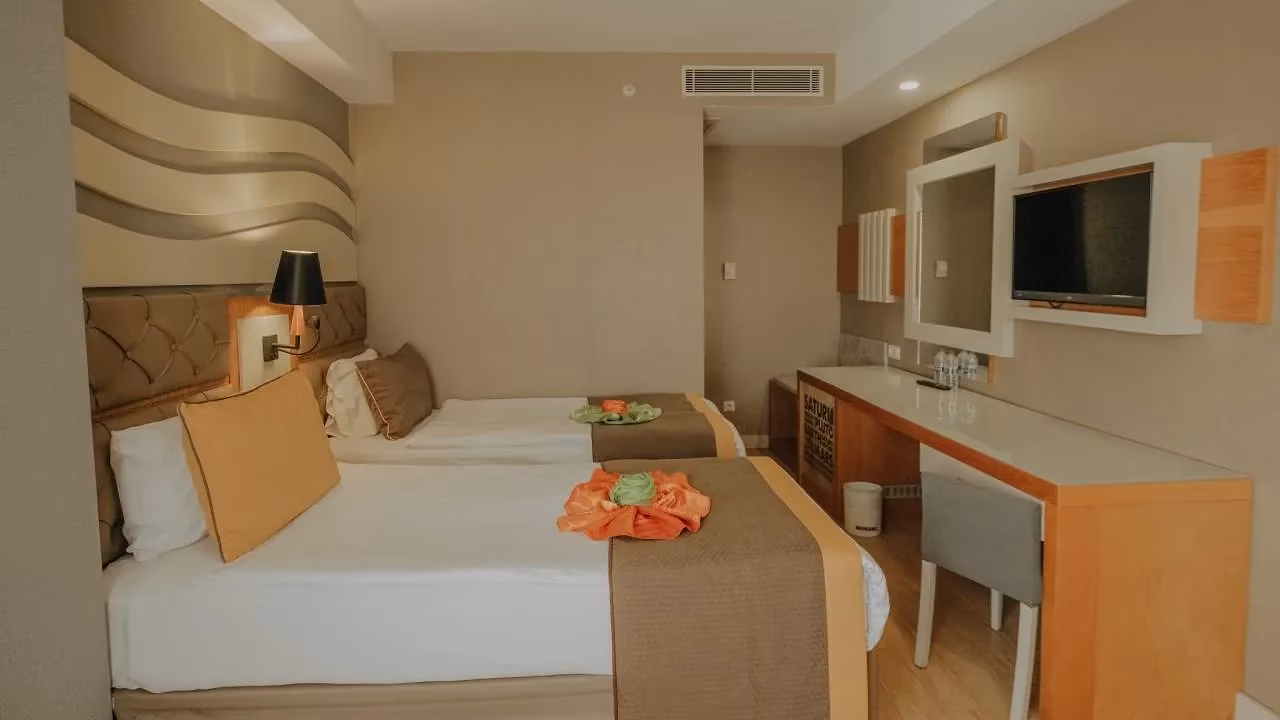 Smalle slaapkamer met twee eenpersoonsbedden en een bureau met tv in Saturn Palace Resort in Lara