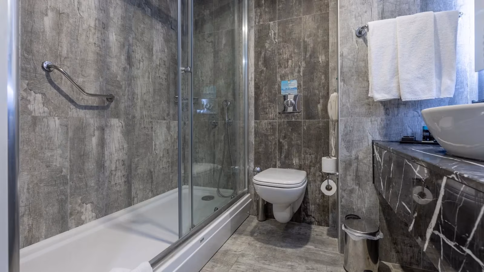 Badkamer met inloopdouche achter glas, toilet en grijze tegels in Saturn Palace Resort