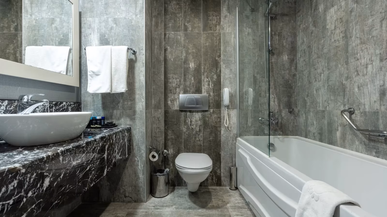 Badkamer met bad, toilet, wastafel op een marmeren blad en grijze tegels in een standaardkamer van Saturn Palace Resort