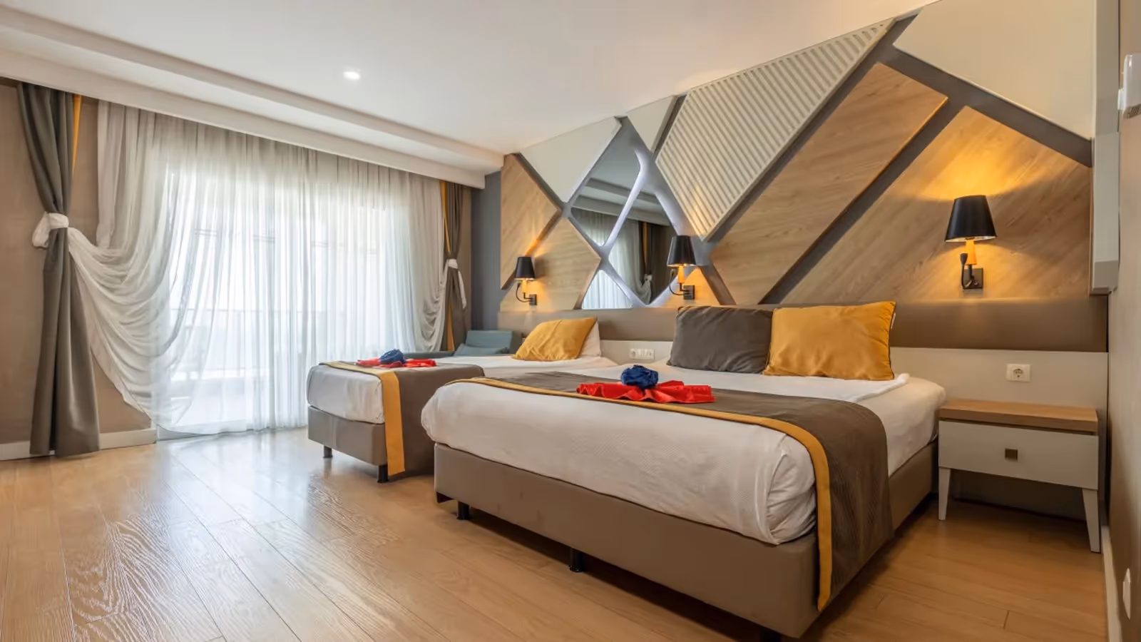 Kamer met een tweepersoonsbed en een eenpersoonsbed, een wand met houten driehoekpanelen en grote ramen in Saturn Palace Resort in Lara
