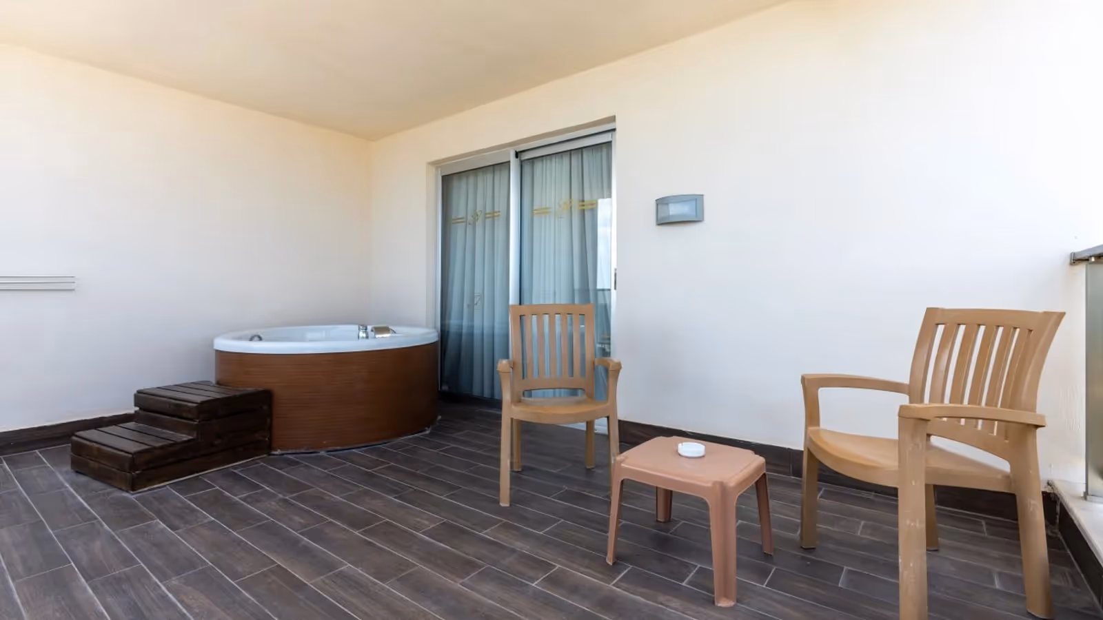 Overdekt terras met een whirlpool, houten stoelen en een bijzettafel in een kamer met terrasjacuzzi in Saturn Palace Resort in Lara