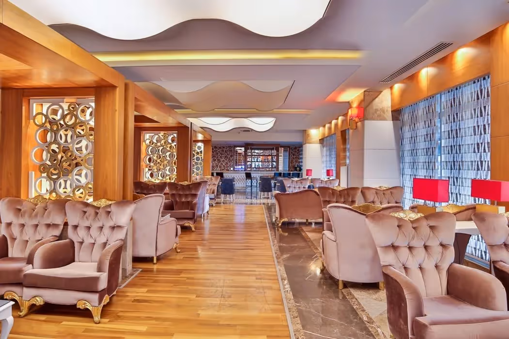 Lounge met roze fauteuils, een parketvloer en rode lampen in Saturn Palace Resort in Lara
