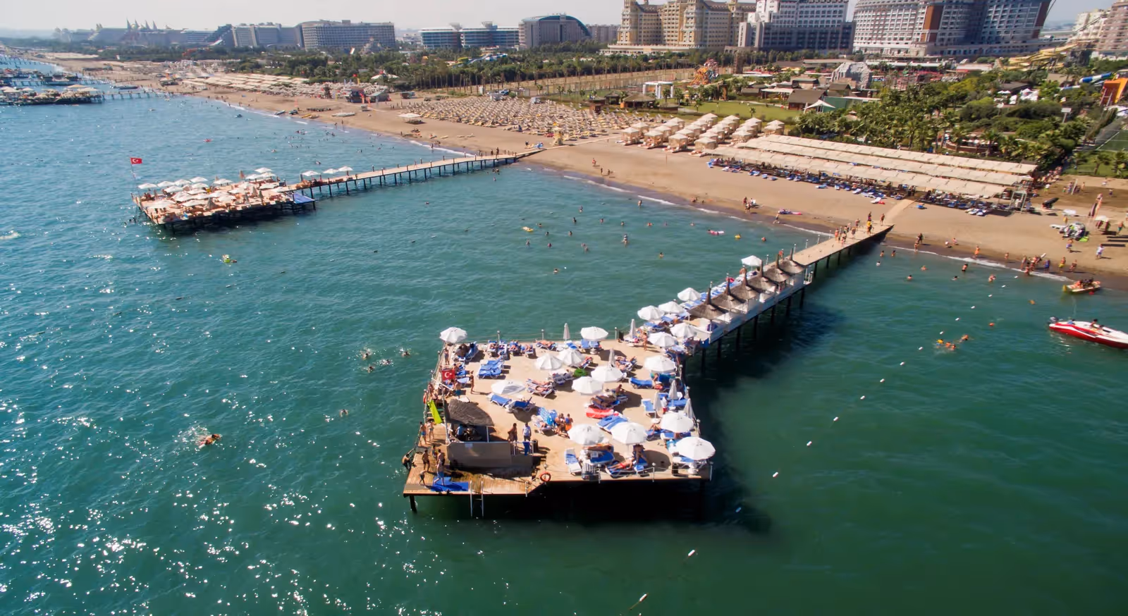 Luchtfoto van het pierplatform met ligbedden en parasols boven helder zeewater bij Saturn Palace Resort in Lara