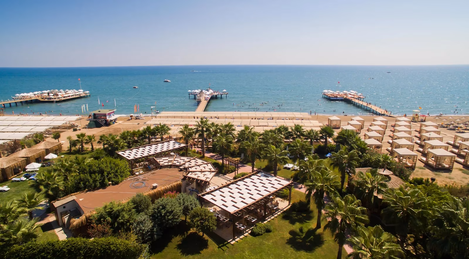 Luchtfoto van de tuin met palmen, het zandstrand met parasols en de pieren in zee bij Saturn Palace Resort