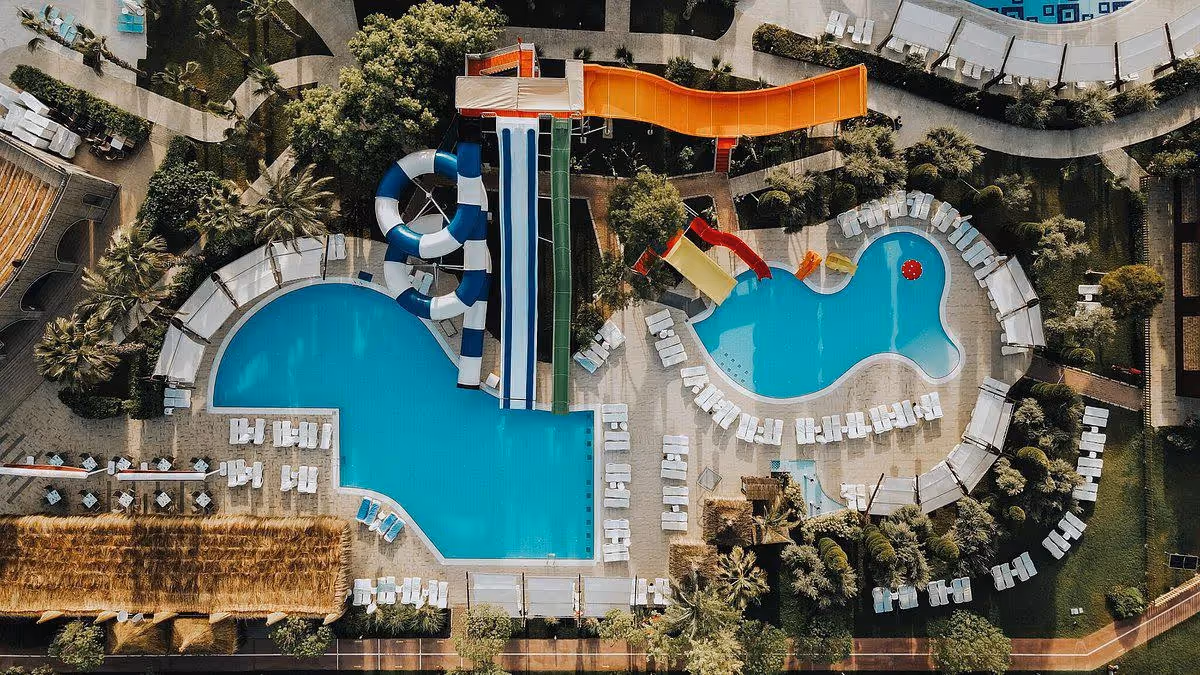 Luchtfoto recht van boven op twee zwembaden met glijbanen en ligbedden eromheen bij Saturn Palace Resort in Lara