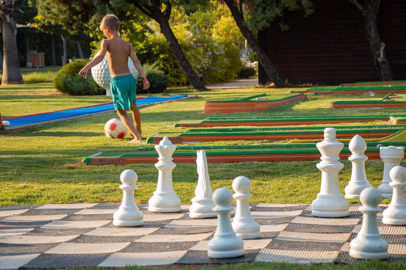 Jongen met een bal naast de minigolfbaan en een groot tuinschaakspel op het gras bij Saturn Palace Resort