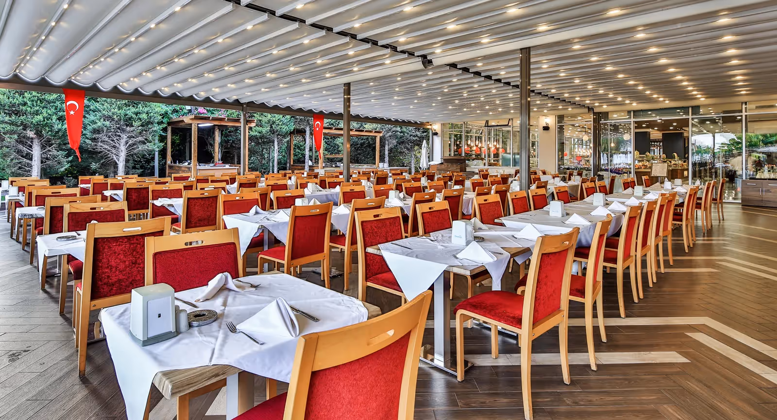 Restaurantzaal met rijen gedekte tafels en rode stoelen onder een overkapping in Saturn Palace Resort in Lara