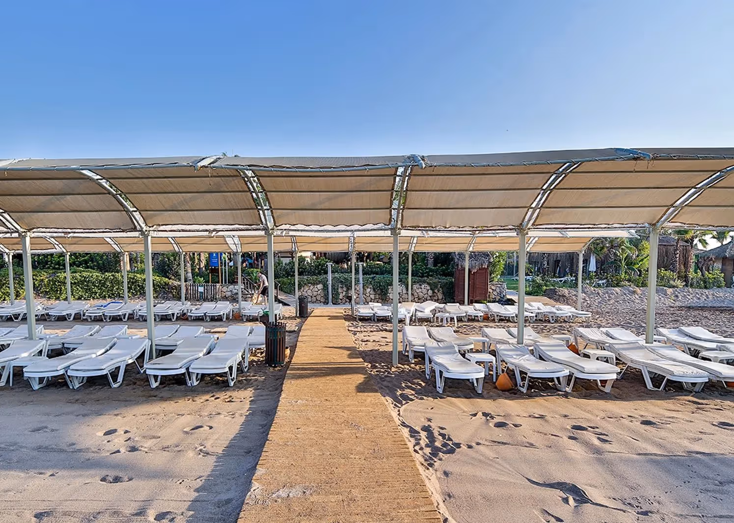 Houten looppad over het zand tussen ligbedden onder schaduwdoeken bij Saturn Palace Resort in Lara