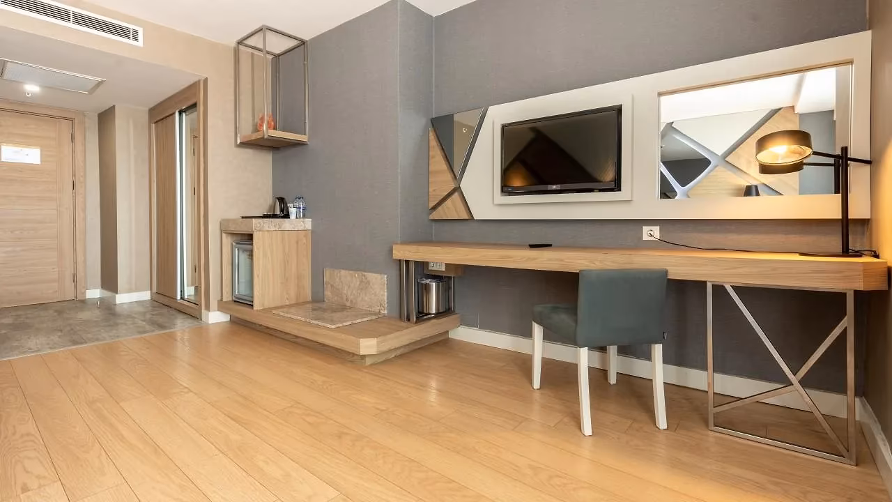 Lichte kamer met parketvloer, bureau met stoel en een tv aan de wand in Saturn Palace Resort in Lara