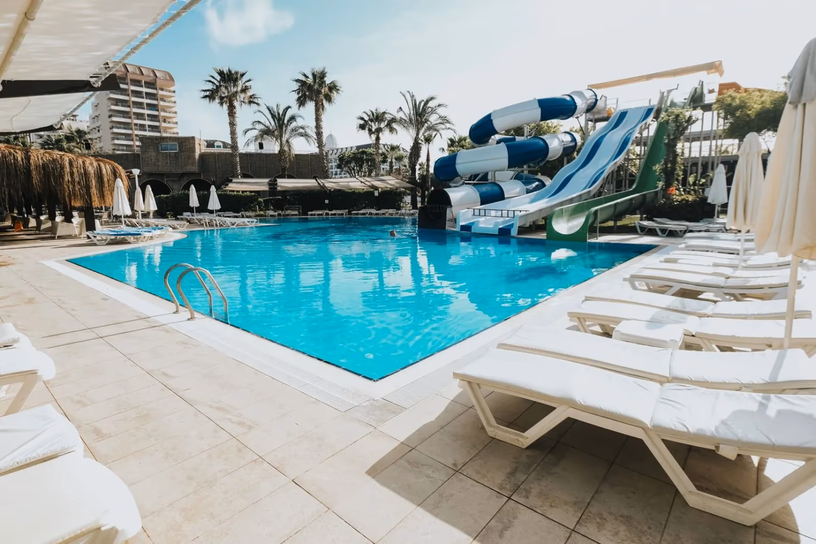 Zwembad met ligbedden op de rand en blauwe en witte glijbanen erachter bij Saturn Palace Resort